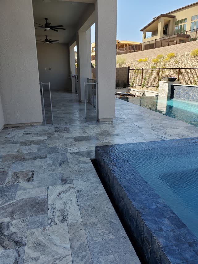 Silver travertine pool deck beside a vanishing-edge spa
